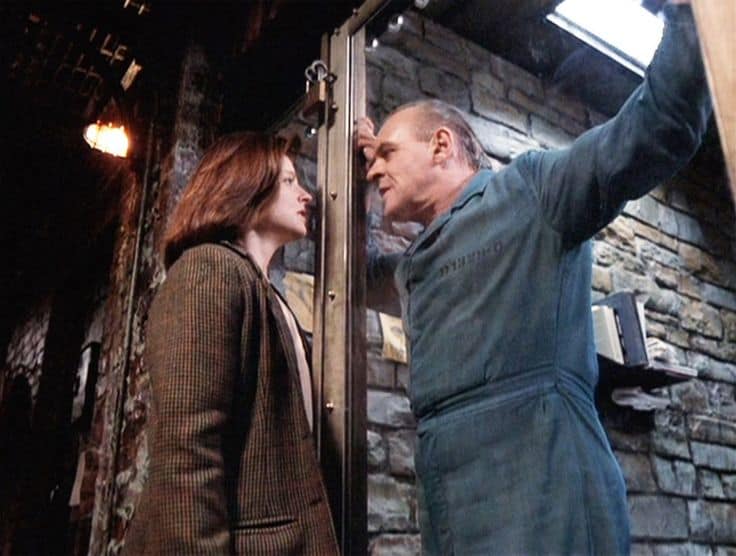 jodie foster y anthony hopkins en una escena del silencio de los corderos. él está dentro de una celda . y mira amenazante al personaje de foster, que parece asustada